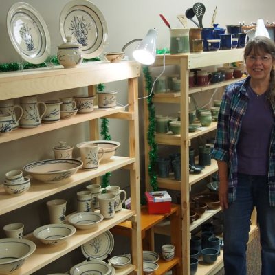 Priya Harding standing beside shelves filled with work at the Guild Holiday sale