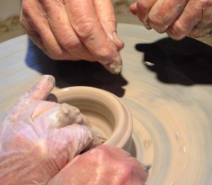 Picture of student hands on clay with teacher's hands nearby for assistance