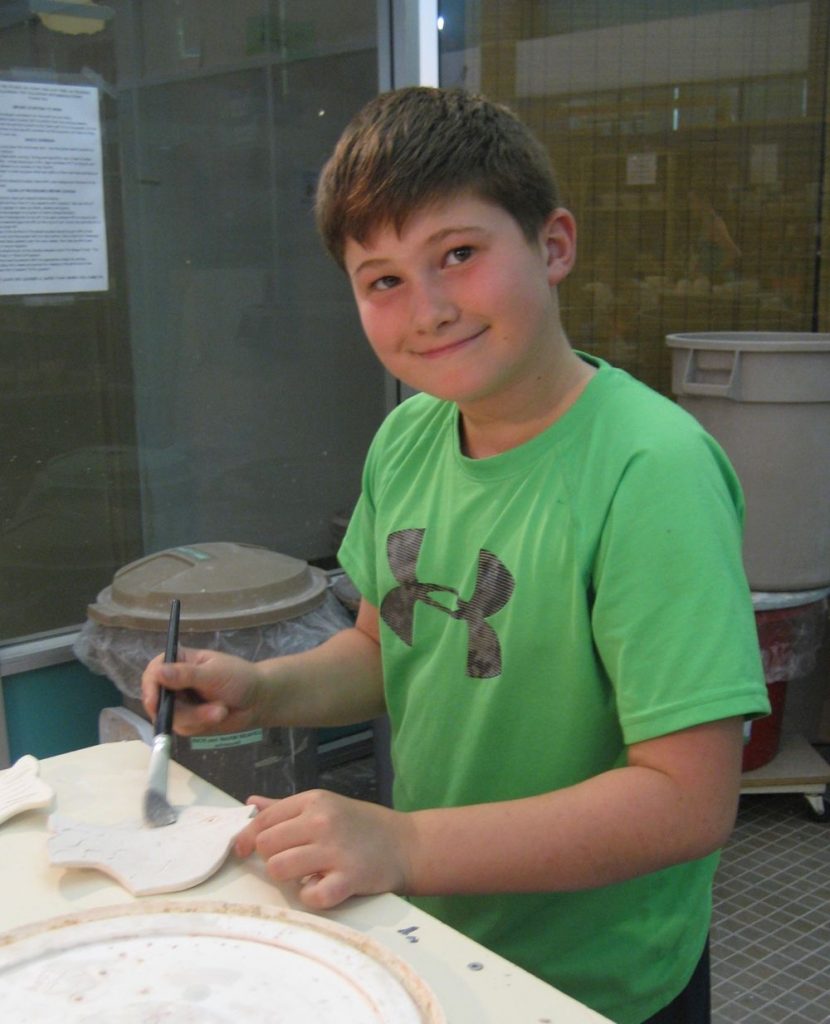 child painting their hand built pottery piece