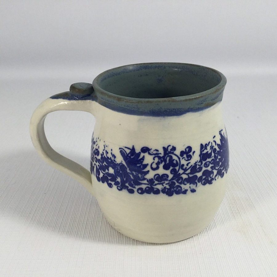 Blue flower stencil wraps around middle of a white clay mug. Glazed matt blue inside - Heather Brooks