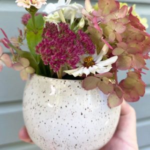 White speckled clay with white glaze round vase holding colourful flowers.  Emily Vail
