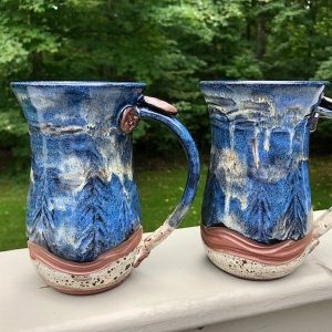Blue wave mugs with tree and cloud like texture and red clay applique buttons at the top of the handles - Sara Purves